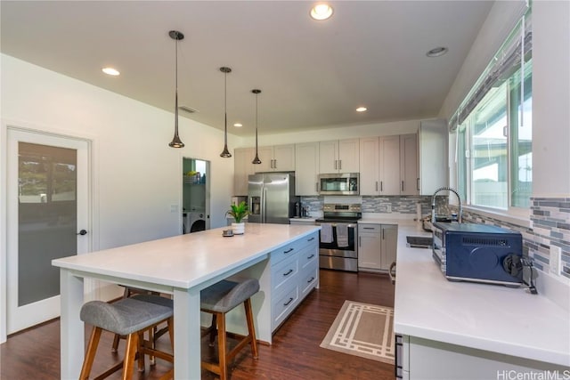 kitchen with stainless steel appliances, independent washer and dryer, decorative light fixtures, decorative backsplash, and a kitchen island