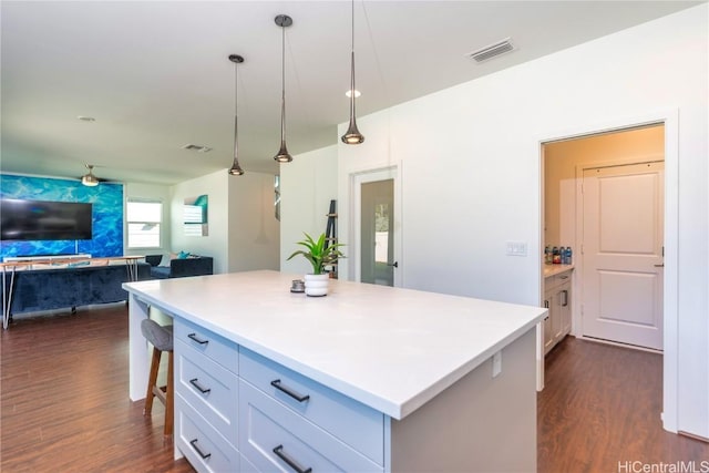 kitchen with white cabinetry, dark wood-type flooring, decorative light fixtures, a kitchen bar, and a kitchen island