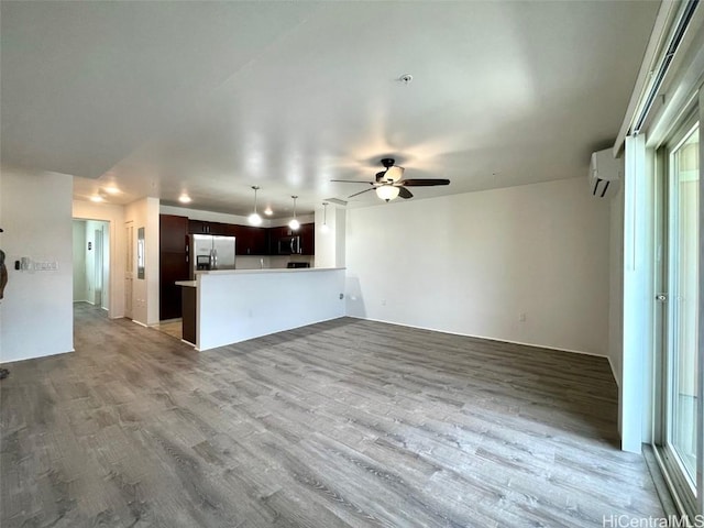 unfurnished living room featuring a wall mounted air conditioner, ceiling fan, and light wood-type flooring