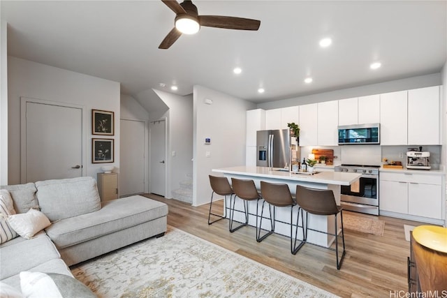 kitchen featuring appliances with stainless steel finishes, white cabinetry, a kitchen breakfast bar, light wood-type flooring, and an island with sink