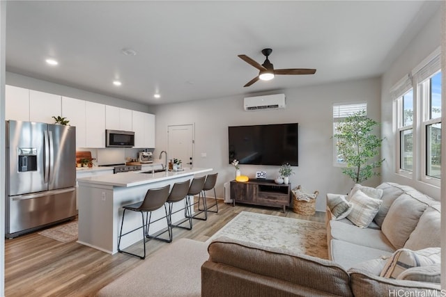 living room with sink, light wood-type flooring, an AC wall unit, and ceiling fan