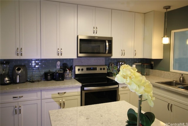 kitchen featuring white cabinetry, sink, backsplash, hanging light fixtures, and stainless steel appliances