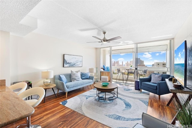 living room with hardwood / wood-style flooring, ceiling fan, a textured ceiling, and a wall of windows