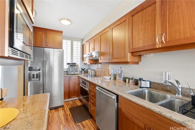 kitchen featuring stainless steel appliances, light stone countertops, sink, and light wood-type flooring