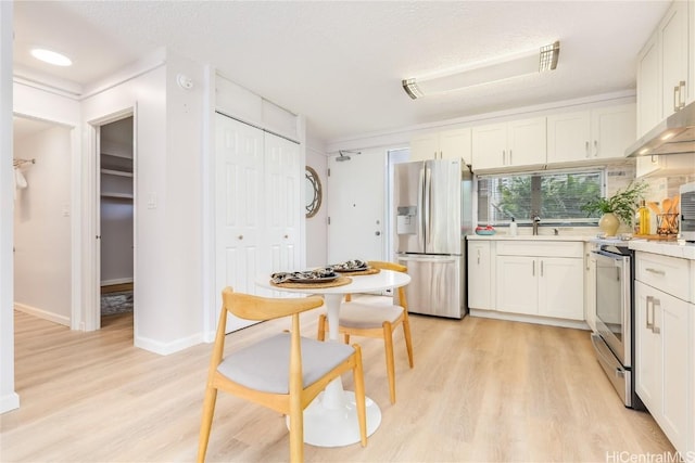 kitchen with appliances with stainless steel finishes, light wood-type flooring, a textured ceiling, sink, and white cabinetry