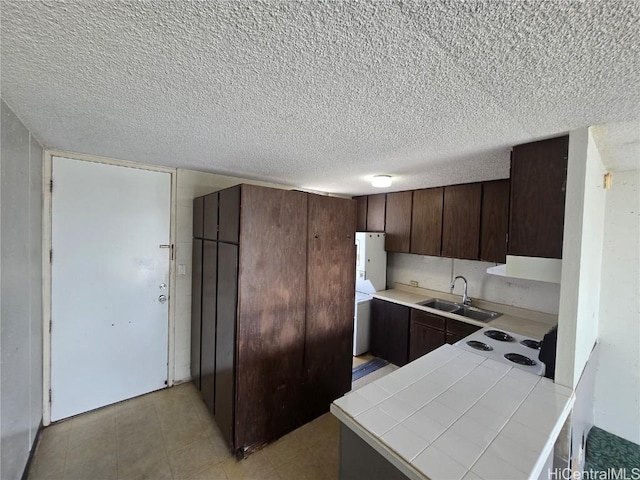 kitchen featuring dark brown cabinetry, sink, white stovetop, tile countertops, and washer / dryer