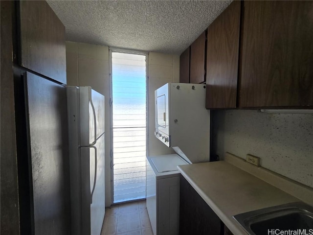 kitchen featuring a textured ceiling, white fridge, stacked washer / drying machine, and sink