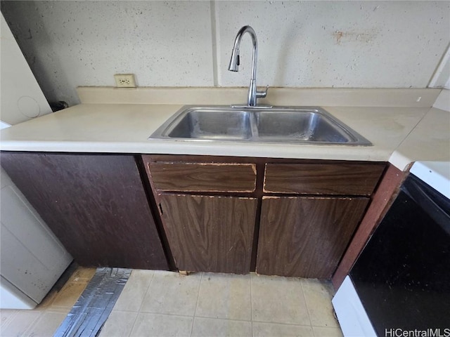 kitchen featuring stove, dark brown cabinetry, sink, and light tile patterned floors