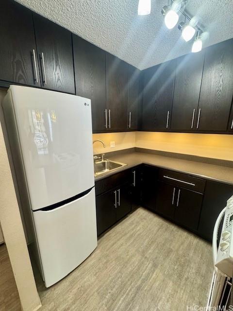 kitchen featuring sink, light hardwood / wood-style floors, a textured ceiling, and white refrigerator