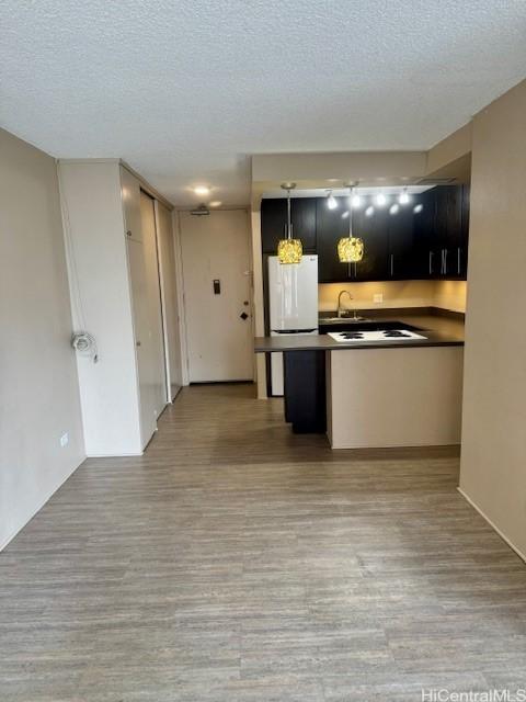 kitchen featuring hanging light fixtures, light hardwood / wood-style floors, a textured ceiling, and white fridge