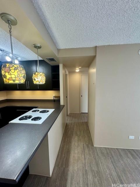 kitchen featuring white stovetop, dark wood-type flooring, hanging light fixtures, and a textured ceiling