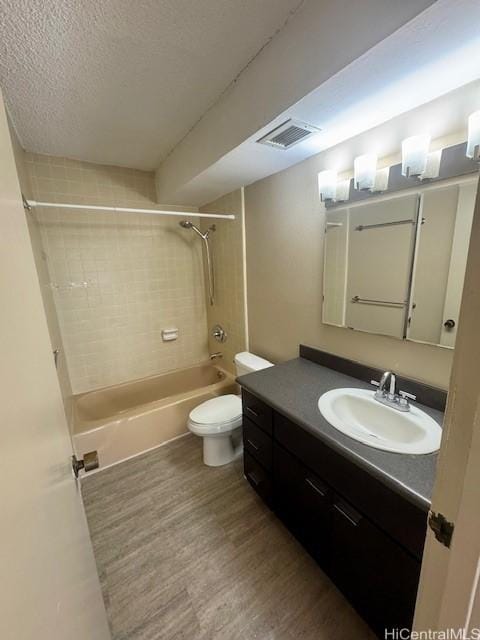 full bathroom with tiled shower / bath combo, vanity, wood-type flooring, a textured ceiling, and toilet