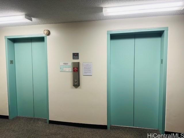 hall with dark colored carpet, elevator, and a textured ceiling