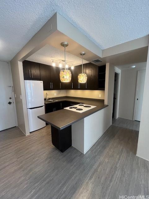 kitchen featuring white appliances, wood-type flooring, kitchen peninsula, and a textured ceiling