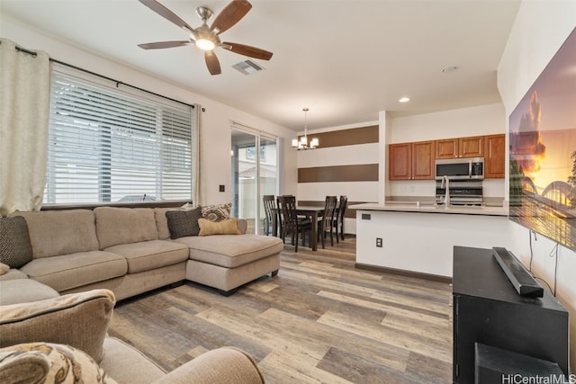 living room with ceiling fan with notable chandelier, sink, and light hardwood / wood-style floors