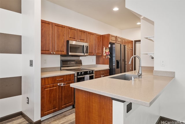 kitchen featuring a kitchen breakfast bar, stainless steel appliances, light wood-type flooring, kitchen peninsula, and sink