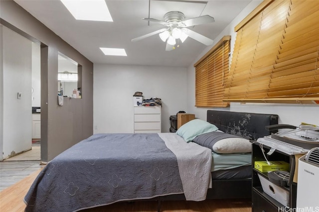 bedroom featuring ceiling fan, a skylight, hardwood / wood-style floors, and connected bathroom