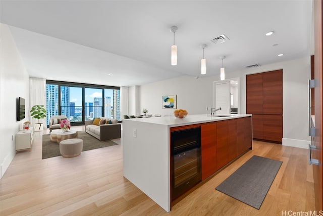 kitchen featuring wine cooler, decorative light fixtures, floor to ceiling windows, a center island with sink, and sink