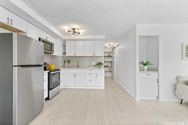 kitchen featuring decorative backsplash, a textured ceiling, stainless steel appliances, sink, and white cabinetry