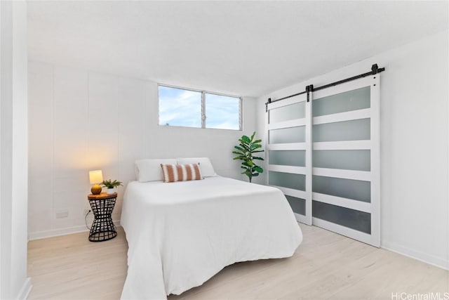 bedroom with a barn door and light hardwood / wood-style floors