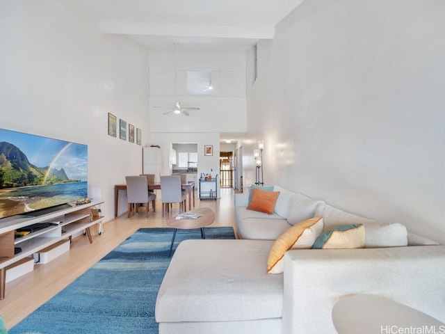 living room featuring beam ceiling, a towering ceiling, ceiling fan, and hardwood / wood-style floors