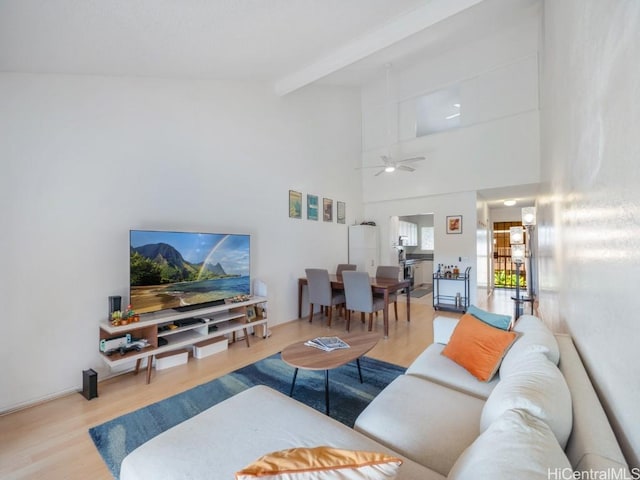 living room with a towering ceiling, ceiling fan, hardwood / wood-style floors, and beamed ceiling