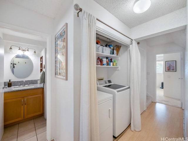 clothes washing area featuring sink, light hardwood / wood-style floors, a textured ceiling, and independent washer and dryer