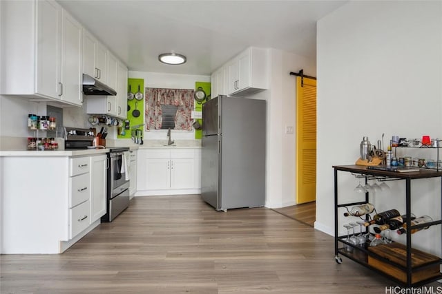 kitchen featuring appliances with stainless steel finishes, sink, a barn door, light hardwood / wood-style flooring, and white cabinets