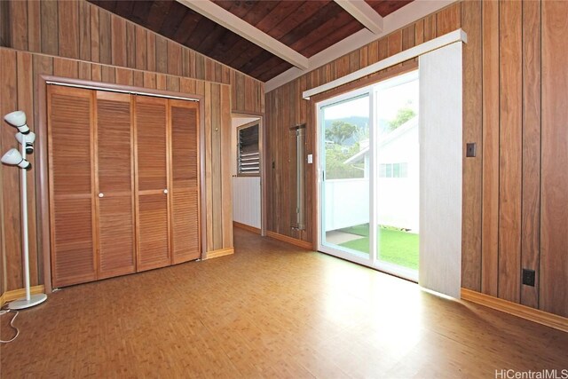 unfurnished bedroom with lofted ceiling with beams, wooden ceiling, access to exterior, wood walls, and a closet