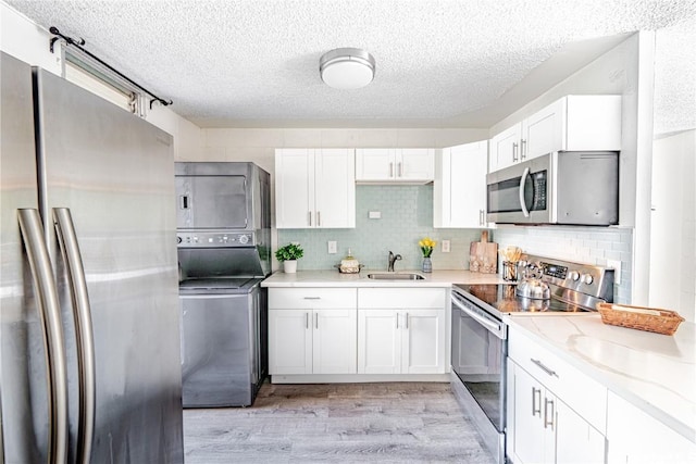 kitchen featuring light hardwood / wood-style floors, stainless steel appliances, stacked washer / dryer, white cabinets, and sink