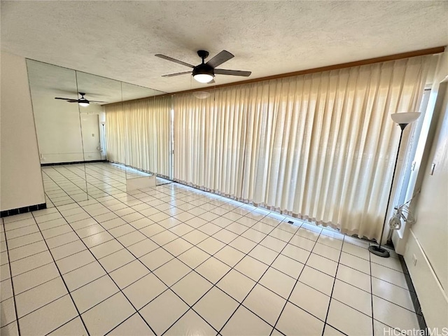 empty room with a textured ceiling, ceiling fan, and light tile patterned flooring