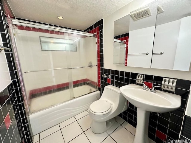 full bathroom featuring toilet, a textured ceiling, tile walls, bath / shower combo with glass door, and tile patterned floors