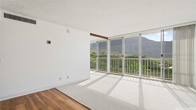 unfurnished room featuring a mountain view, wood-type flooring, a textured ceiling, and floor to ceiling windows