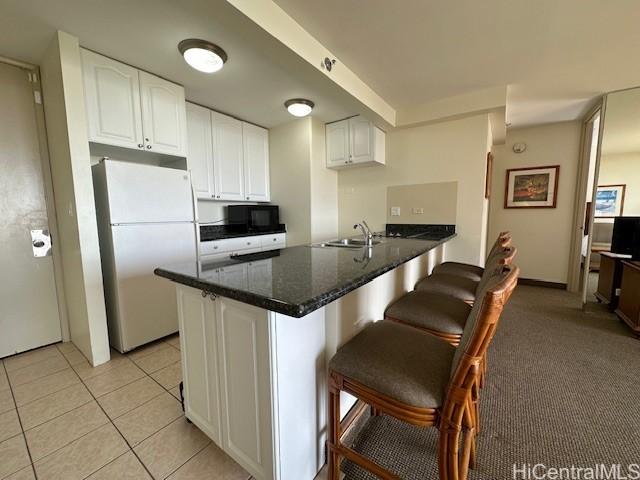 kitchen with white fridge, kitchen peninsula, a kitchen bar, and white cabinetry