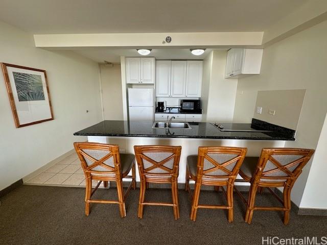 kitchen with kitchen peninsula, white refrigerator, white cabinets, and a kitchen breakfast bar