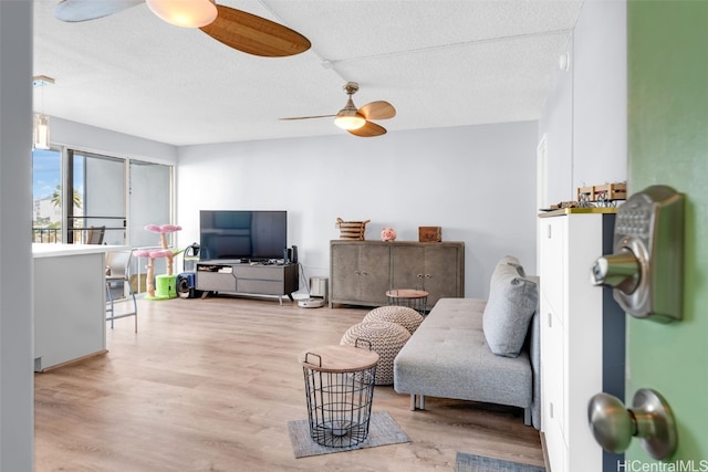 living room featuring ceiling fan, a textured ceiling, and light hardwood / wood-style flooring