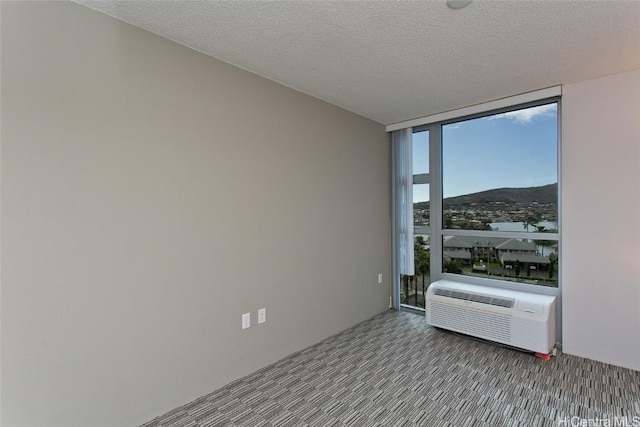 unfurnished room featuring floor to ceiling windows, a textured ceiling, cooling unit, and a mountain view