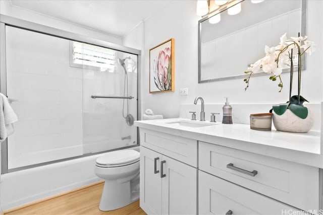 bathroom featuring vanity, toilet, wood finished floors, and shower / bath combination with glass door