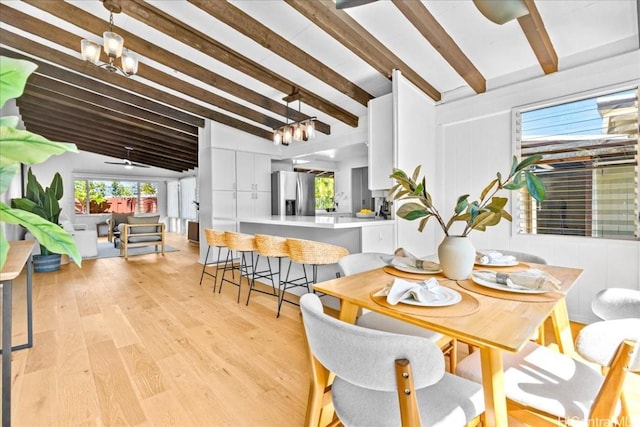 dining room featuring lofted ceiling with beams, light wood-style floors, and a chandelier