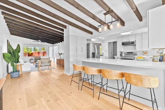 kitchen with light countertops, white cabinetry, appliances with stainless steel finishes, a peninsula, and light wood-style floors