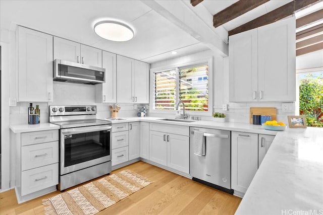 kitchen with a sink, stainless steel appliances, beam ceiling, and light countertops