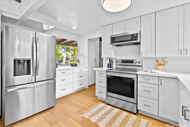 kitchen with light wood finished floors, appliances with stainless steel finishes, tasteful backsplash, and light countertops