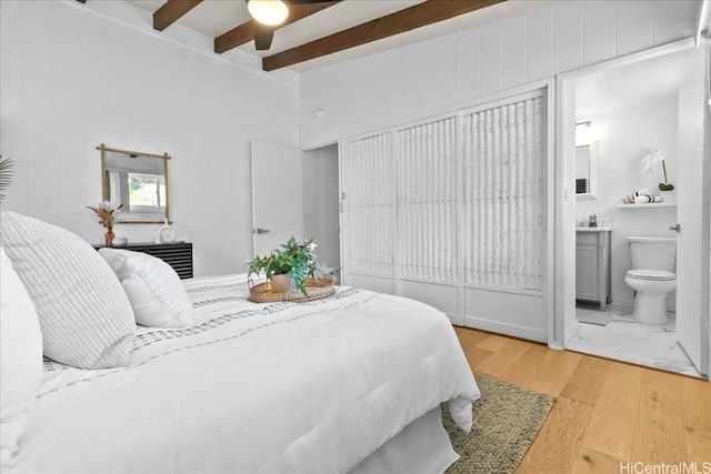 bedroom with a ceiling fan, beamed ceiling, wood finished floors, and connected bathroom