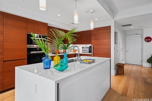 kitchen featuring a center island with sink, wall oven, light wood-type flooring, pendant lighting, and oven