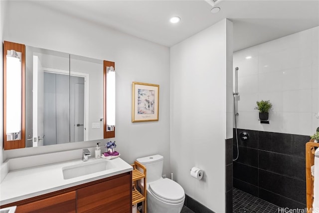 bathroom with toilet, tiled shower, and vanity