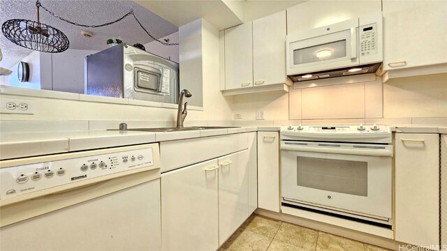 kitchen featuring white appliances, hanging light fixtures, light tile patterned floors, sink, and white cabinets