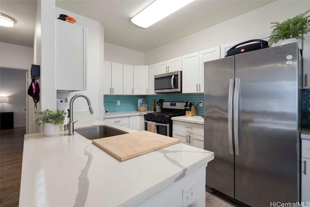 kitchen featuring sink, white cabinetry, light stone counters, stainless steel appliances, and backsplash