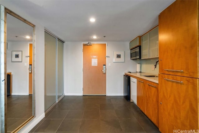 kitchen featuring brown cabinets, light countertops, stainless steel microwave, glass insert cabinets, and a sink