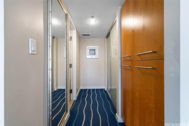 hallway with visible vents, dark carpet, and baseboards