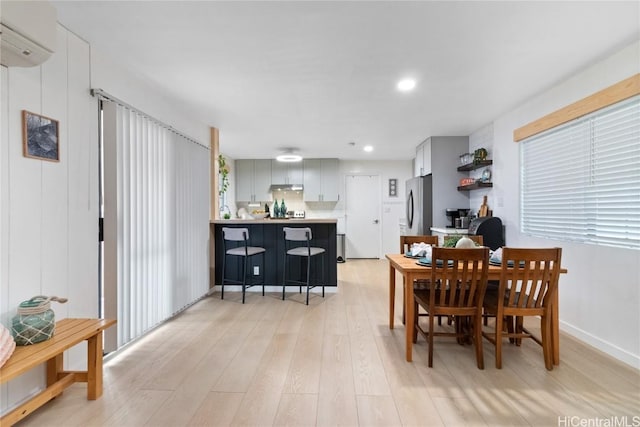 dining area with a wall mounted AC and light wood-type flooring